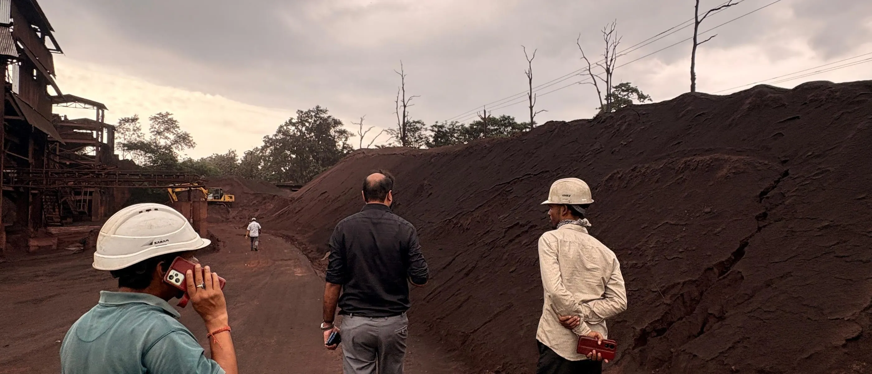 Brikway personnel in hard hats walking a haul road between stockpiles of ore, with a processing plant behind.